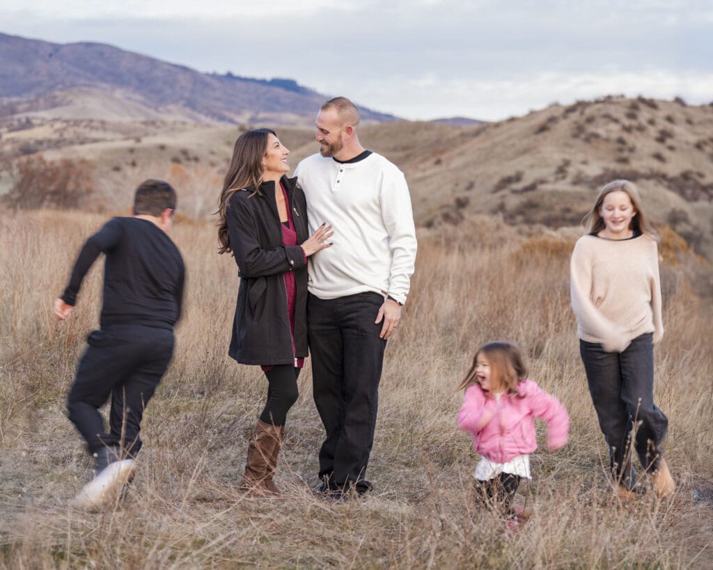Candid outdoor family portrait session in a scenic field during golden hour featuring parents and three children during a Moon Portrait session with Boise Lunar Love photographer
