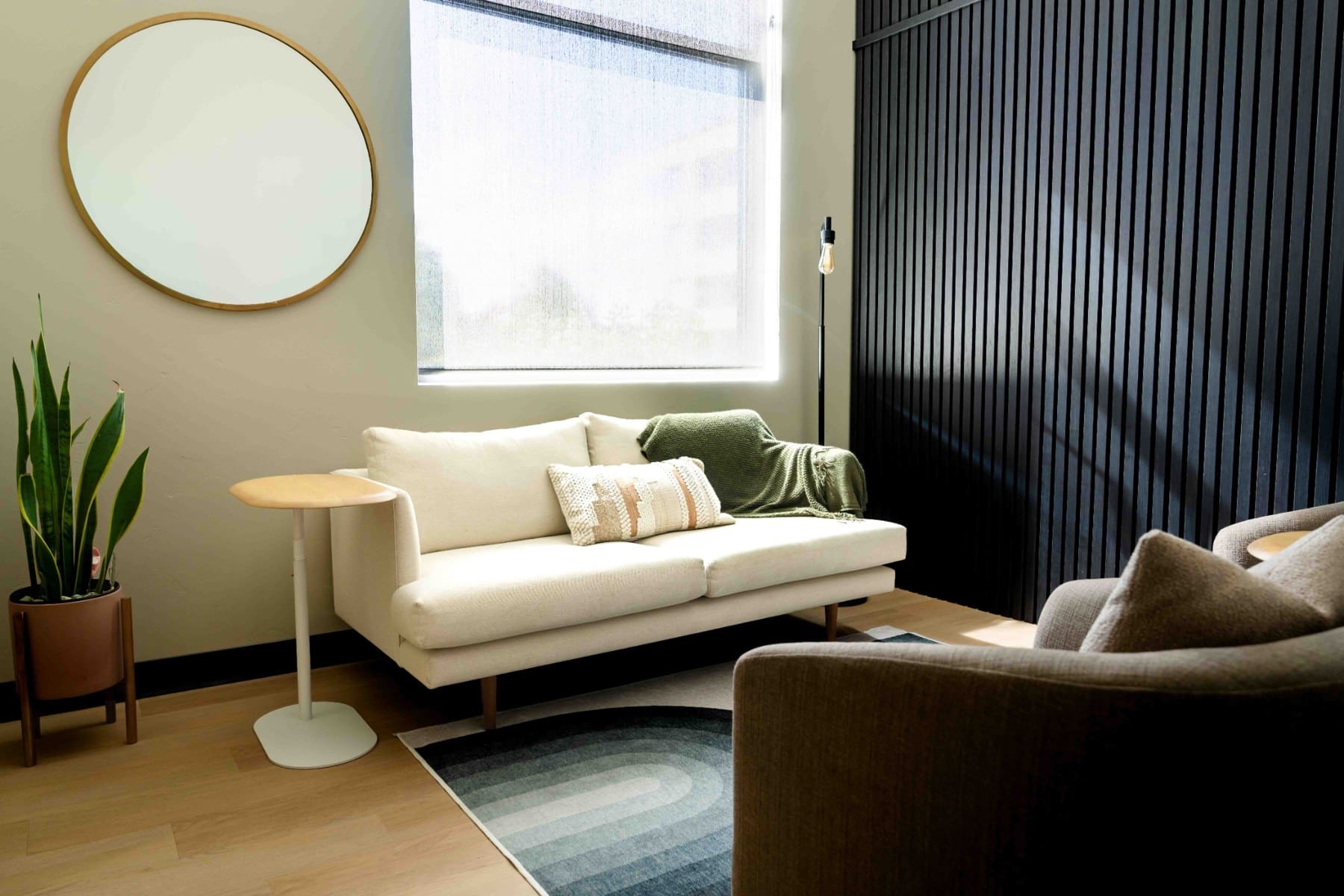 Wide view of a waiting room with a cream sofa, round mirror, and plant