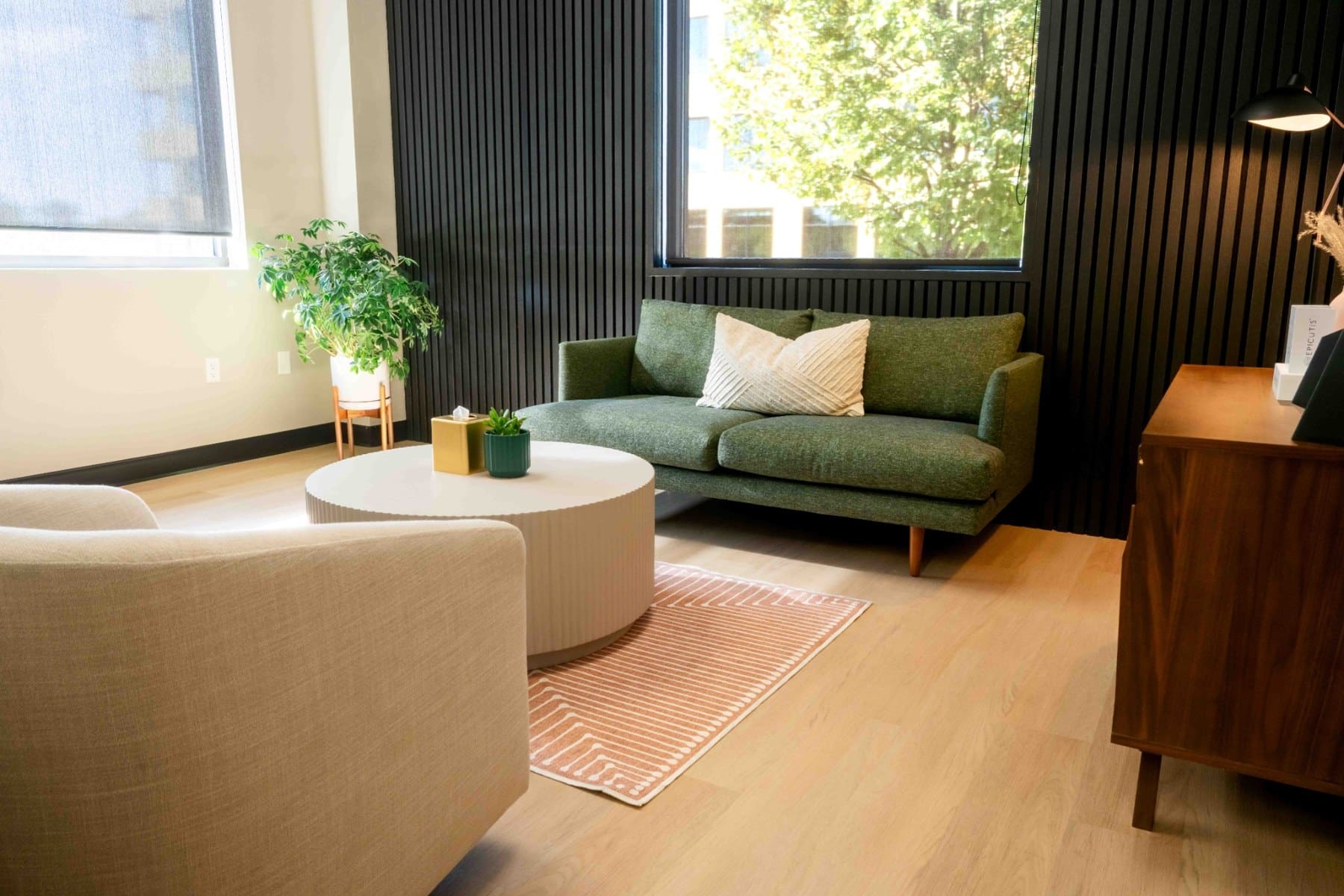Waiting area with a green sofa, round coffee table, and natural window light
